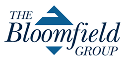 Logo for The Bloomfield Group. The text is in dark blue with "The" and "Group" in smaller caps, and "Bloomfield" in large font. Above the "B" is a triangular design also in blue.
